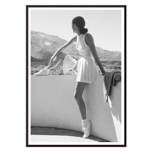 Fashion model in tennis outfit seated on wall looking at mountains by Toni Frissell poster artwork, with black aluminium frame on white background