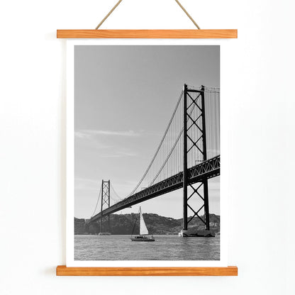 Lisbon Bridge Black and White Poster by Raphael Alves featuring a framed photograph of a suspension bridge and sailboat in the water, with wooden magnetic frame on white background