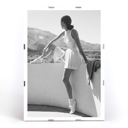 Fashion model in tennis outfit seated on wall looking at mountains by Toni Frissell poster artwork, framed and displayed in modern living room decor