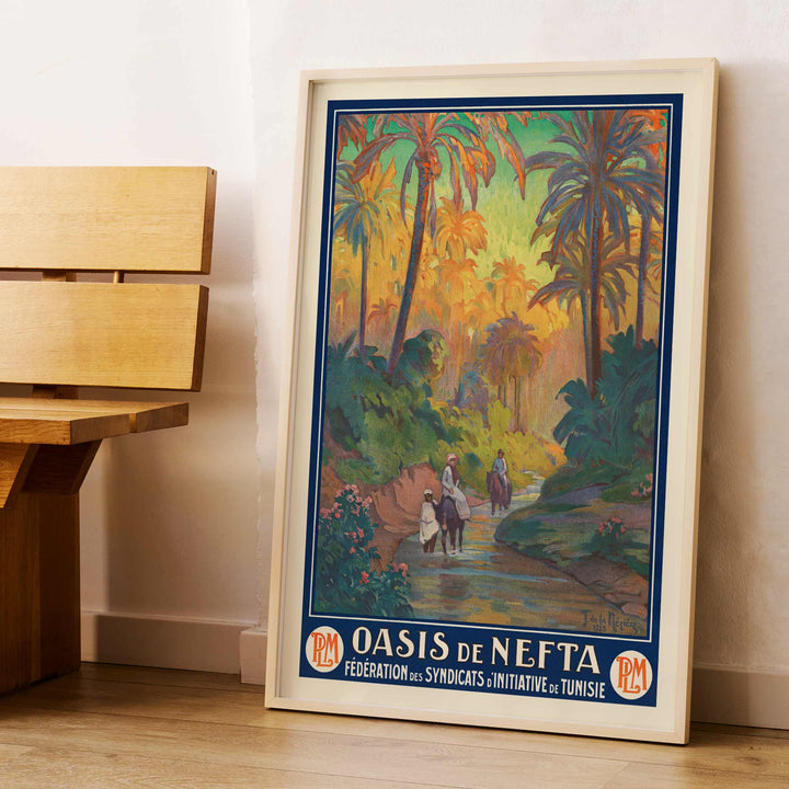 Oasis de Nefta poster by Joseph de La Nézière with lush palm oasis, warm sunset light, figures and winding stream, framed and displayed in modern living room decor