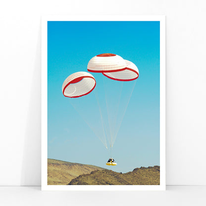 CST-100 crew capsule landing with three parachutes over desert landscape by NASA and The Boeing Company poster artwork, framed and displayed in modern living room decor