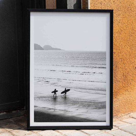 Black and white poster of surfers walking along the beach Surfers walking on the beach artwork, framed and displayed in home decor