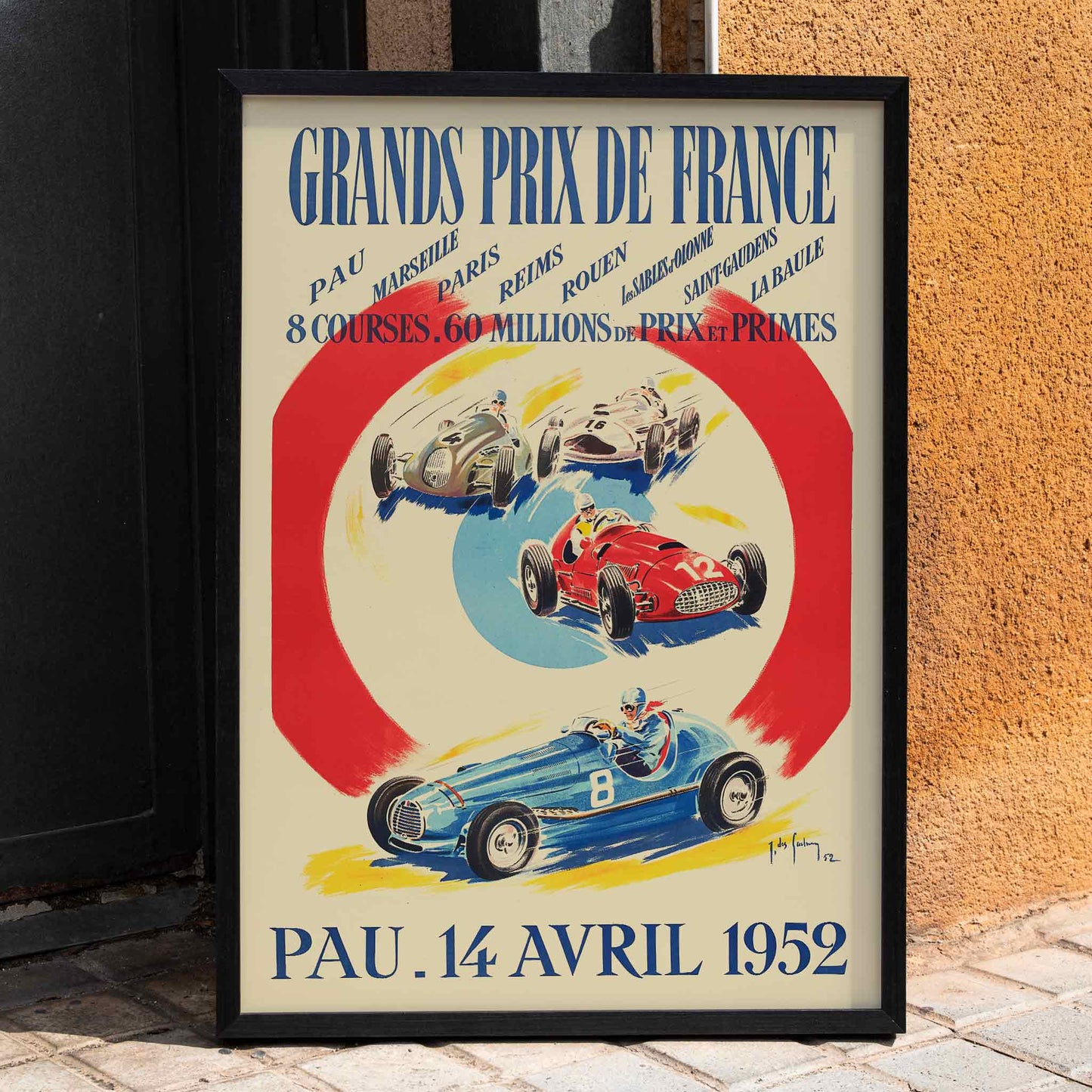 Vintage poster by Jean Des Gachons showing colorful race cars and event details for Grands Prix de France at multiple locations, framed and displayed in home decor