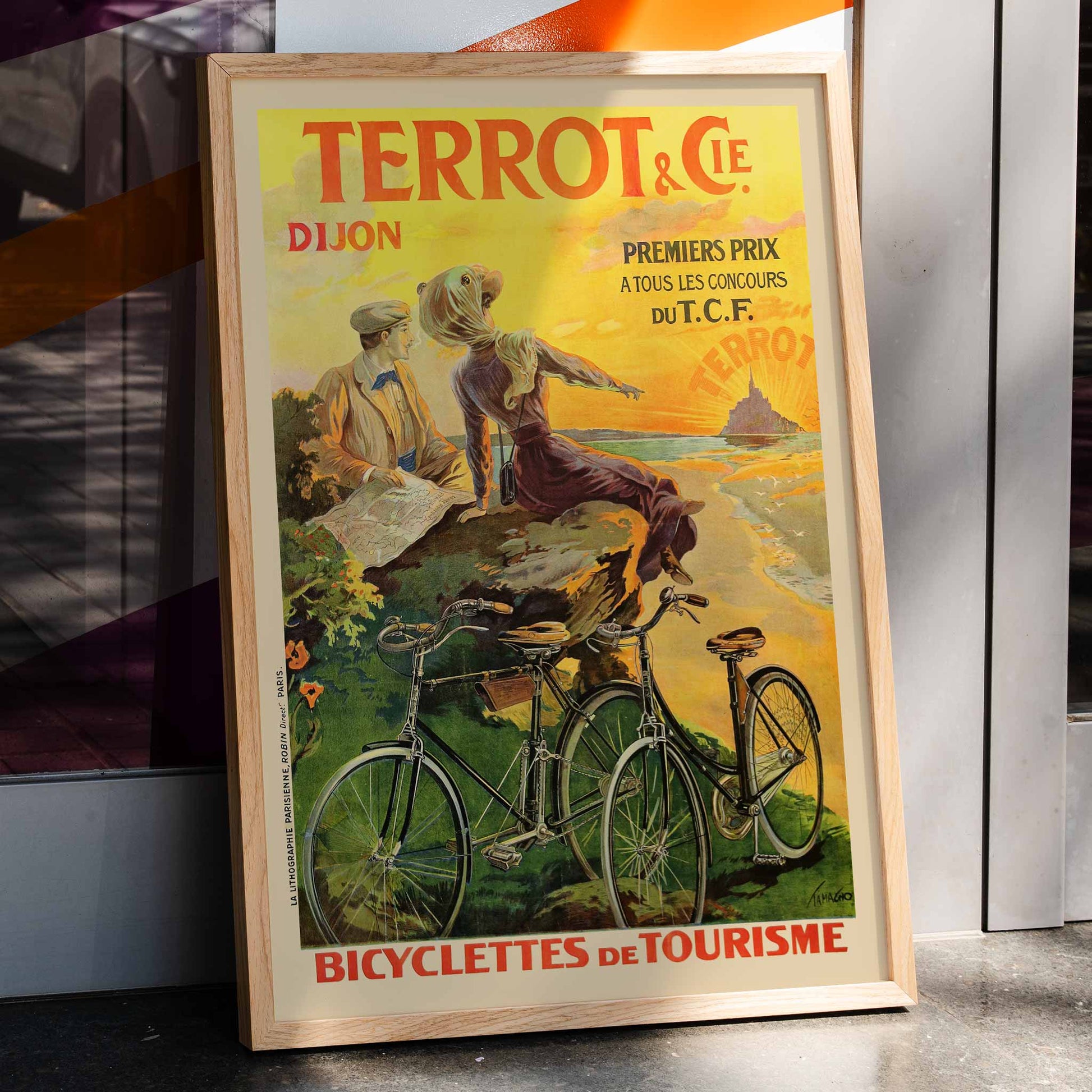 Vintage poster Terrot And Cie Dijon Bicyclettes De Tourisme by Armand Masson showing a couple with touring bicycles overlooking the coast at sunset, framed and displayed in home decor